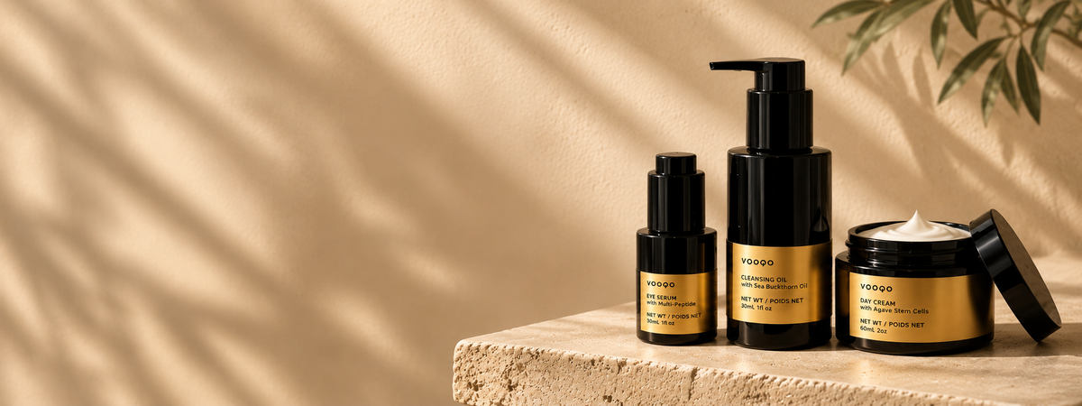 Vooqo cleansing oil, eye serum and open day cream displayed on a travertine pedestal against a warm beige background with soft sunlight.