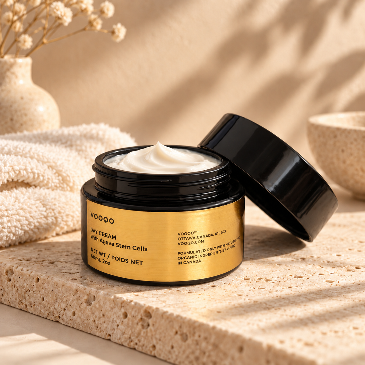 Vooqo Day Cream with Agave Stem Cells in an open black and gold jar with cream, styled on warm travertine.