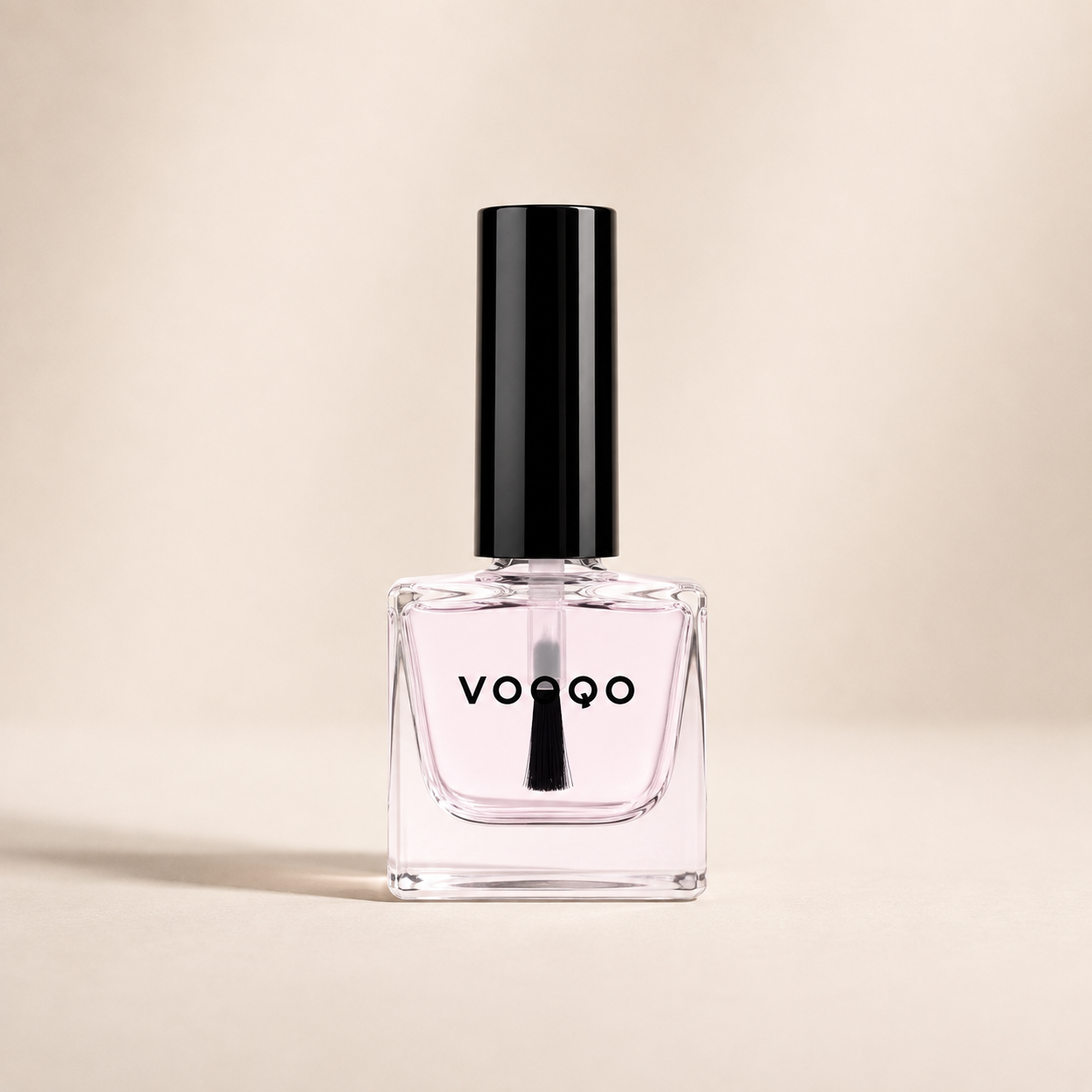 Vooqo Nail Base Coat in a clear glass bottle with pale pink formula on a warm ivory background